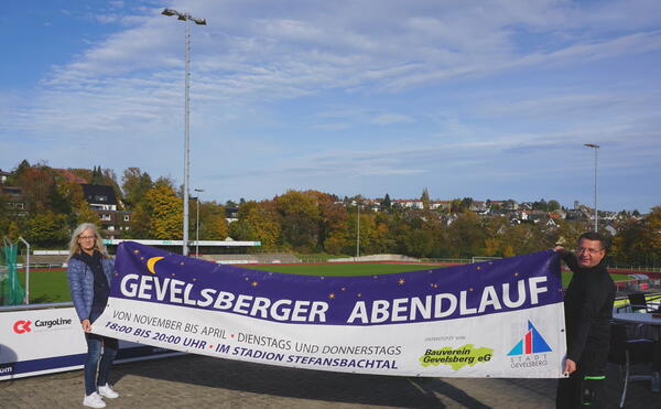 Sie freuen sich auf den Abendlauf: Sportsachbearbeiterin Anette Figge-Kinner und Nikolai Markiw vom Stadionteam mit dem Banner für die Veranstaltungen im Stefansbachtal.